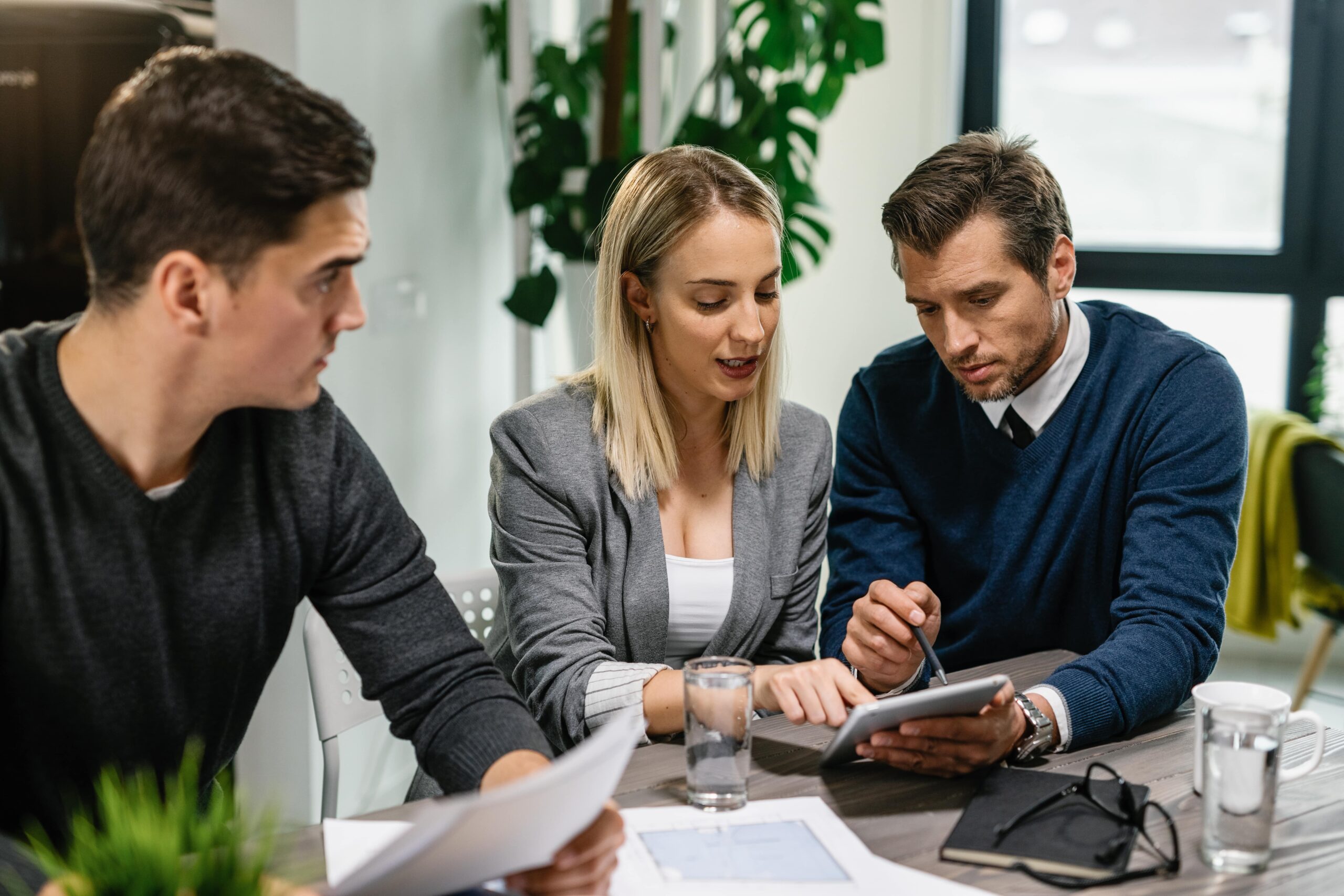 rear estate agent young couple going through housing plans touchpad while having meeting home